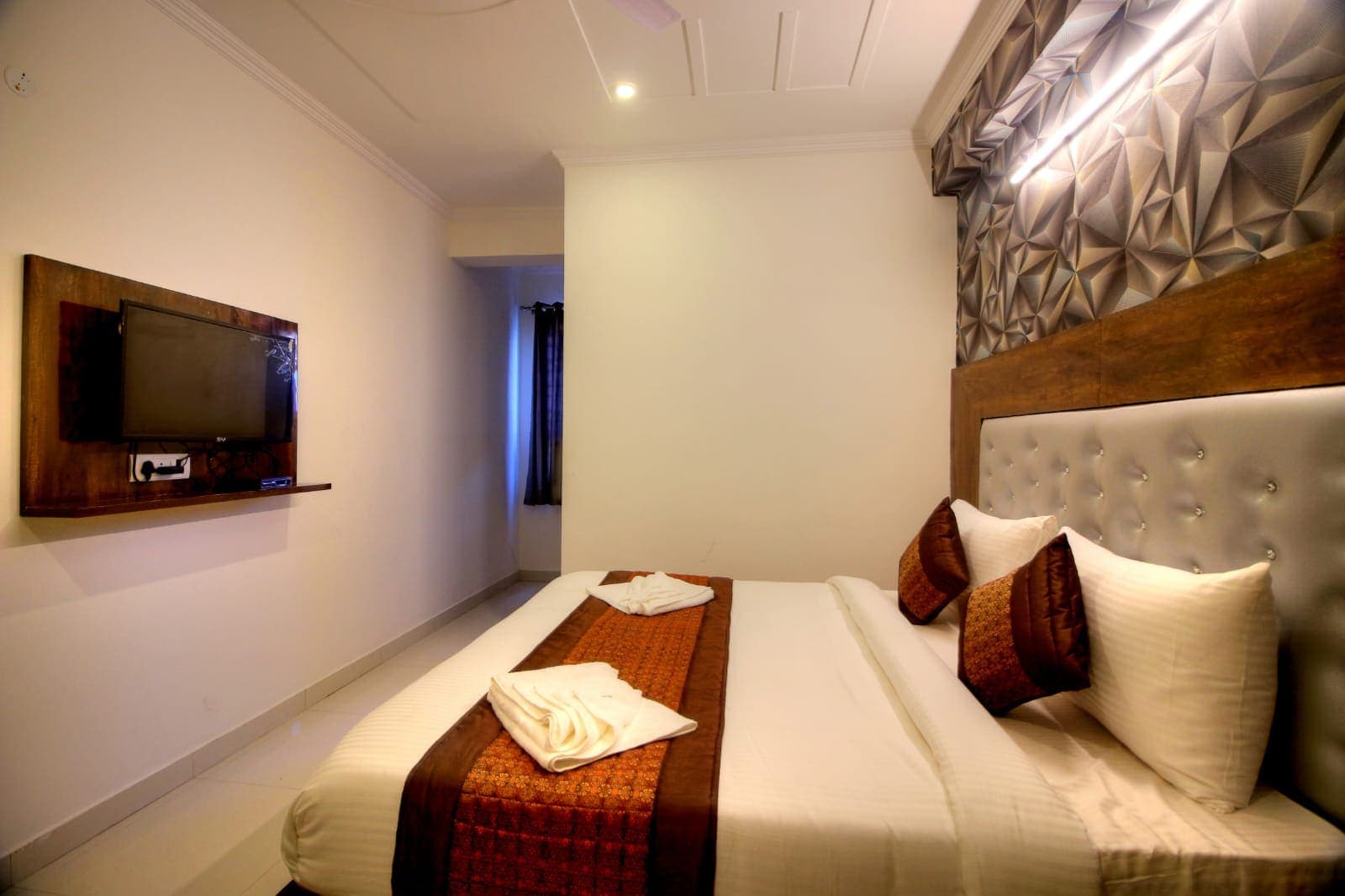 Guest room with a white bed, warm brown accents, and geometric wall panels